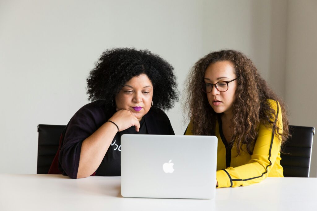 Two women collaborating on recruiting for a role while reviewing LinkedIn profiles of candidates on a laptop 