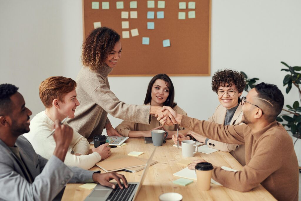 Team members shaking hands with new employee during a meeting, illustrating the importance of optimizing your profile on LinkedIn as a job seeker to attract recruiters and land a new job