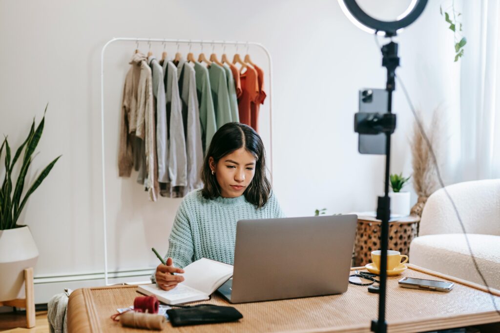 Woman using her laptop for optimizing her LinkedIn profile and job searching and writing down notes in her journal