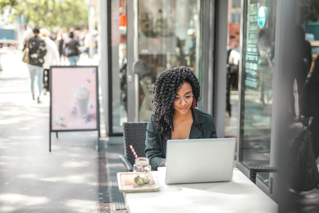 Woman using her laptop for job searching and optimizing her LinkedIn profile while sitting outside a cafe and a drink on the table