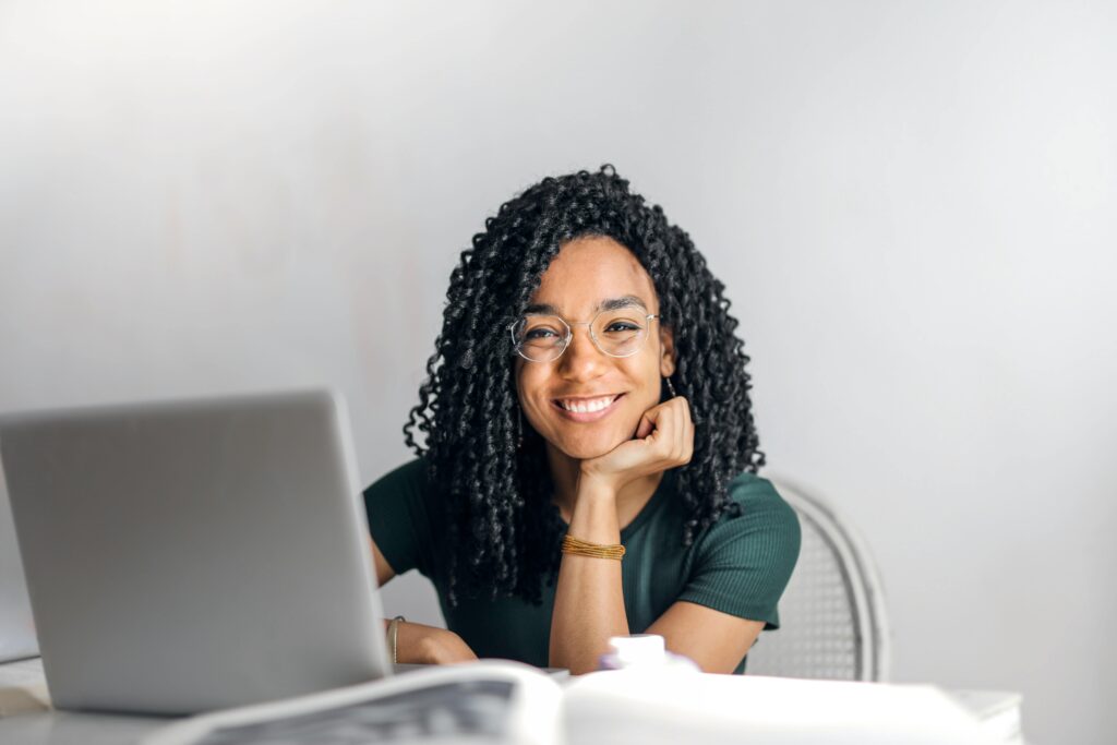 Woman smiling at camera while using her laptop for optimizing her LinkedIn profile.