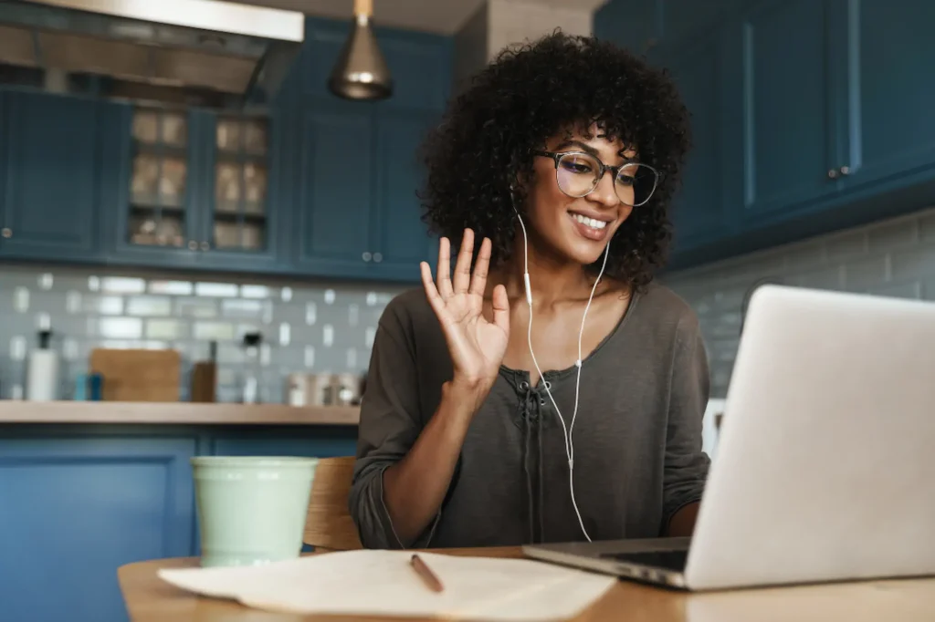 Young Black female entrepreneur on a video call from her home kitchen, smiling and waving