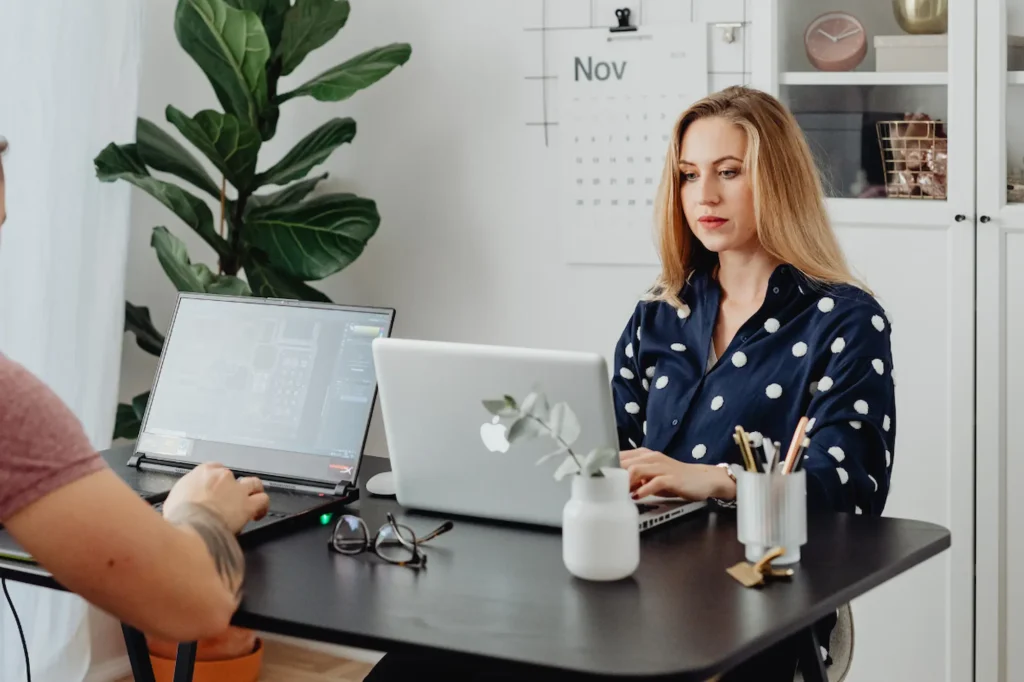 Two people working on laptops at a shared desk in a bright home office setting, improving their business website’s SEO.