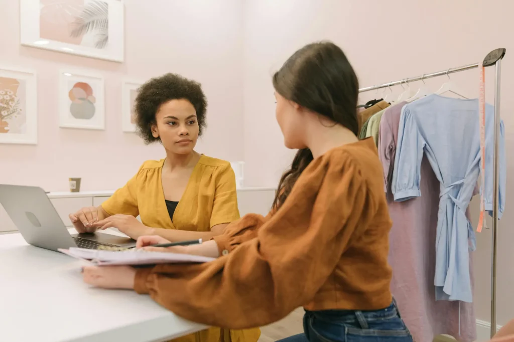 Two women collaborating for their small business, with one seated at a computer while the other sits opposite reviewing their SEO strategy together.