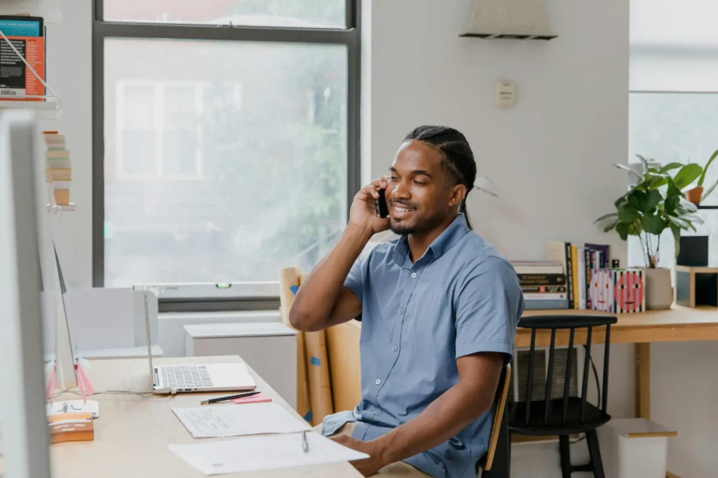 Black male business owner in his office setting, talking on the phone about setting up a PPC campaign for his small business.