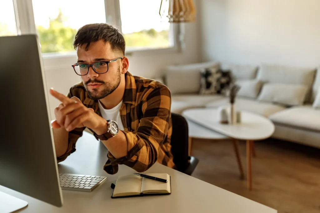 Man with glasses pointing at his computer screen while planning blog ideas and content strategy at his home office desk