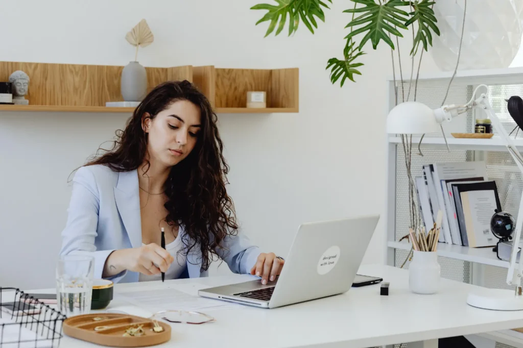 Woman small business owner writing blog content at her desk while working on her laptop in a bright minimalist home office