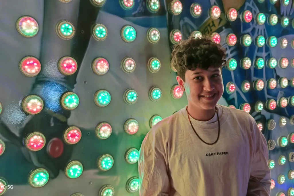 Marketing by Rocio founder smiling in front of a colourful wall of lights, representing queer visibility and identity