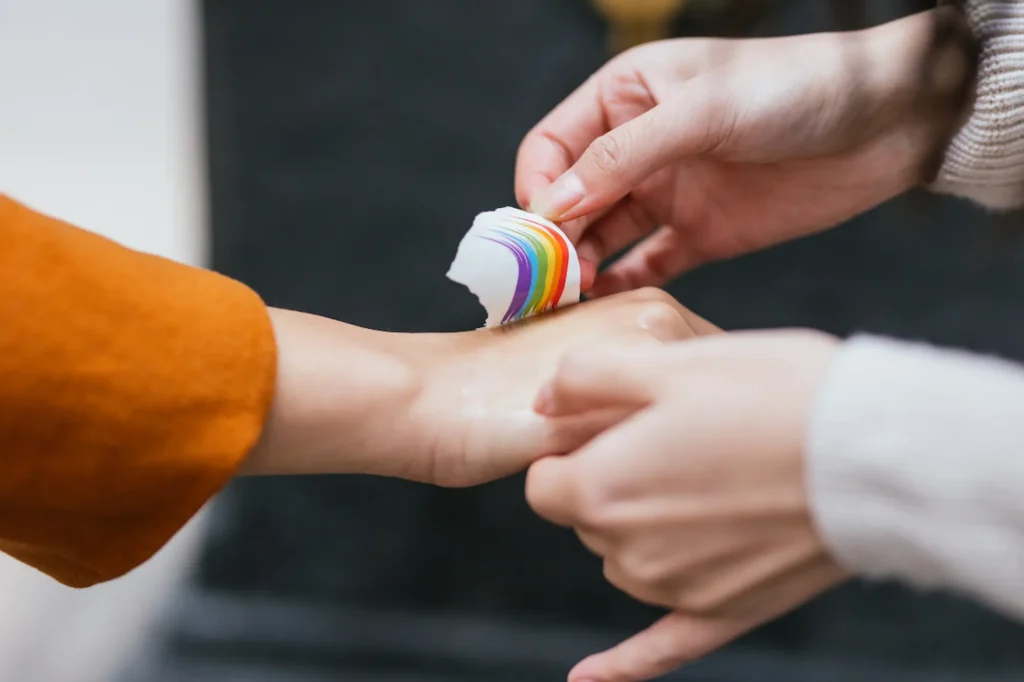 Hands gently placing a rainbow sticker on skin, representing LGBTQ+ pride and solidarity