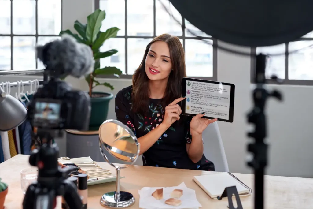 Content creator filming a makeup video and holding up a tablet showing viewer comments
