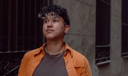 Rocio Sanchez walking confidently wearing an orange button down shirt.